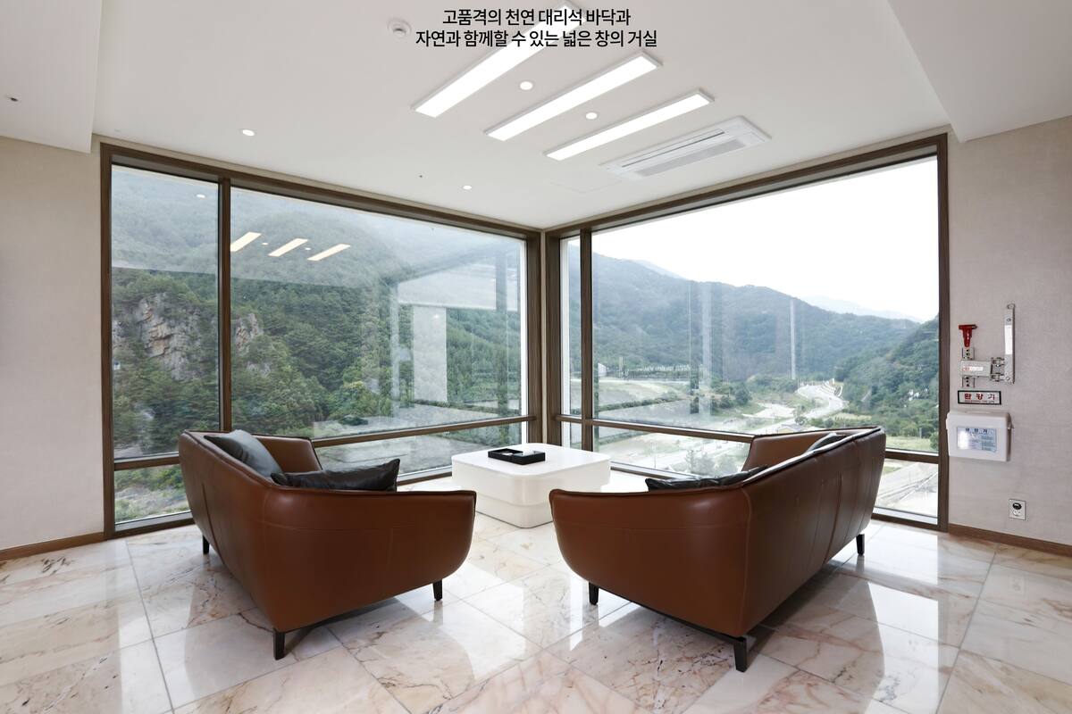 A modern room with large windows, two brown leather sofas, a white coffee table, and a view of a mountainous landscape.