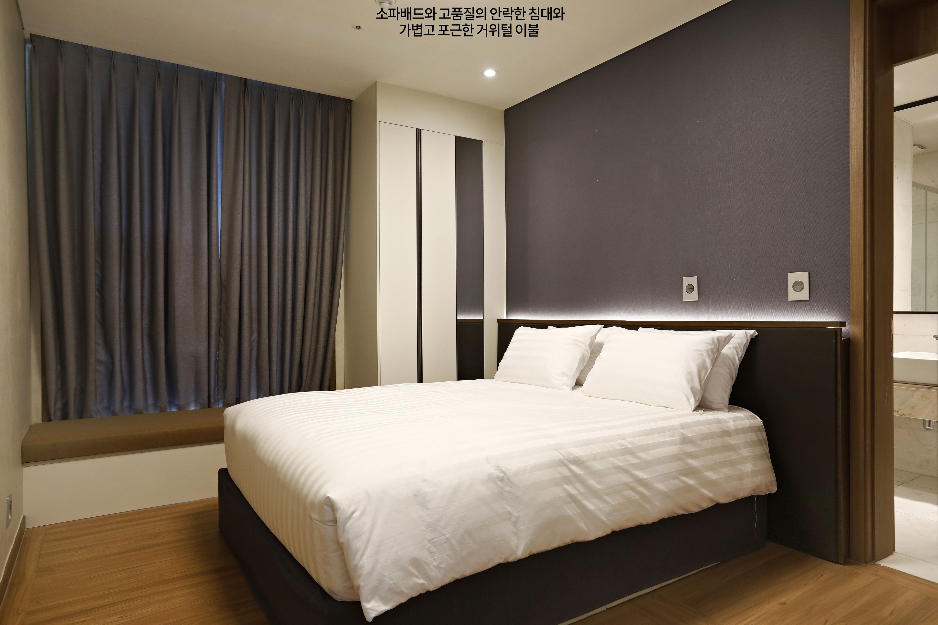 Un dormitorio moderno con una cama grande, una ventana con cortinas y una pared oscura.