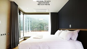 A modern hotel room with a large bed, a view of a forested area, and a balcony. - Pine Forest (Jeongseon)
