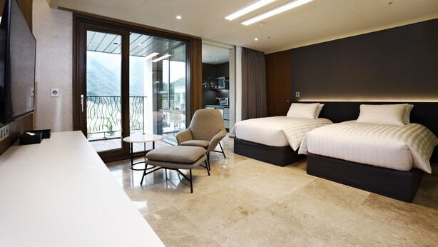 A modern hotel room with a large bed, a desk, a chair, and a balcony with a view. - Pine Forest (Jeongseon)