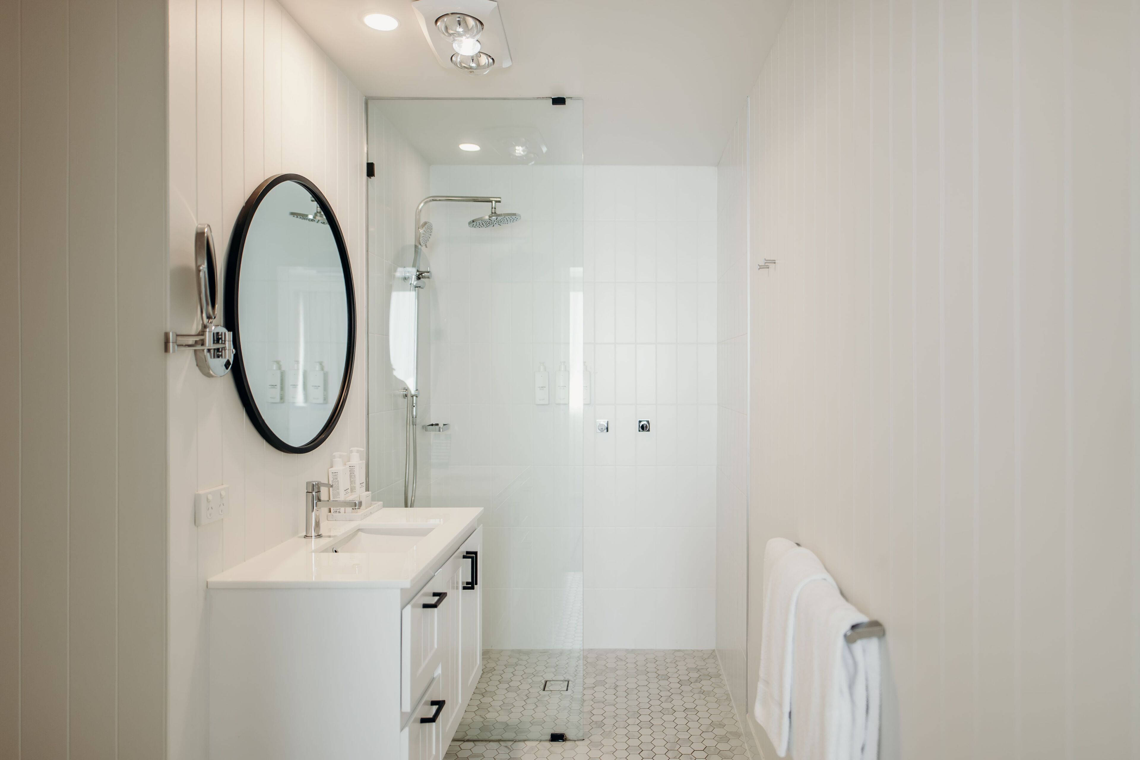 Une salle de bain moderne avec un meuble-lavabo blanc, un grand miroir, une douche et un porte-serviettes.