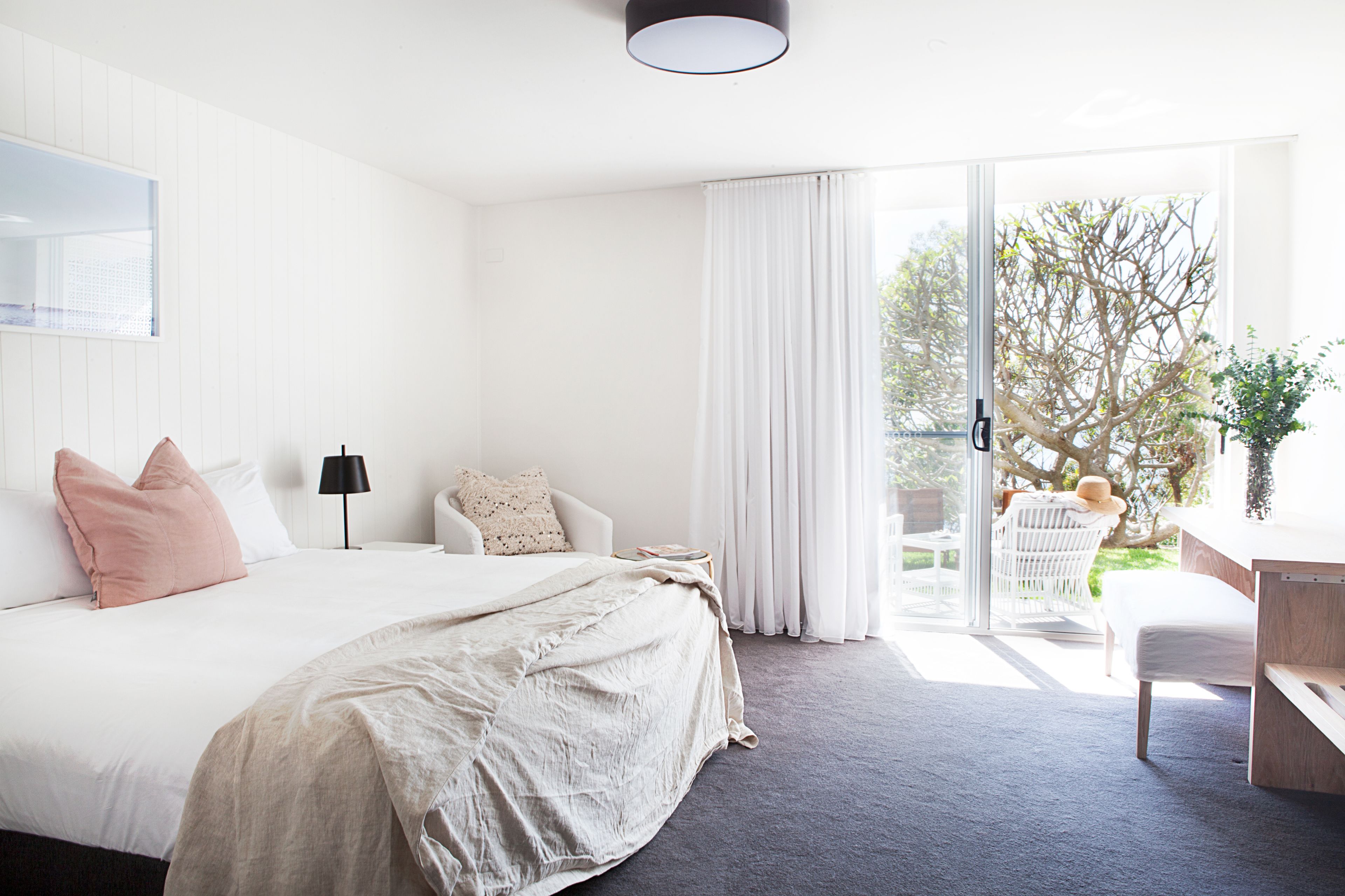 A bedroom with a large bed, a desk, and a view of the outdoors.
