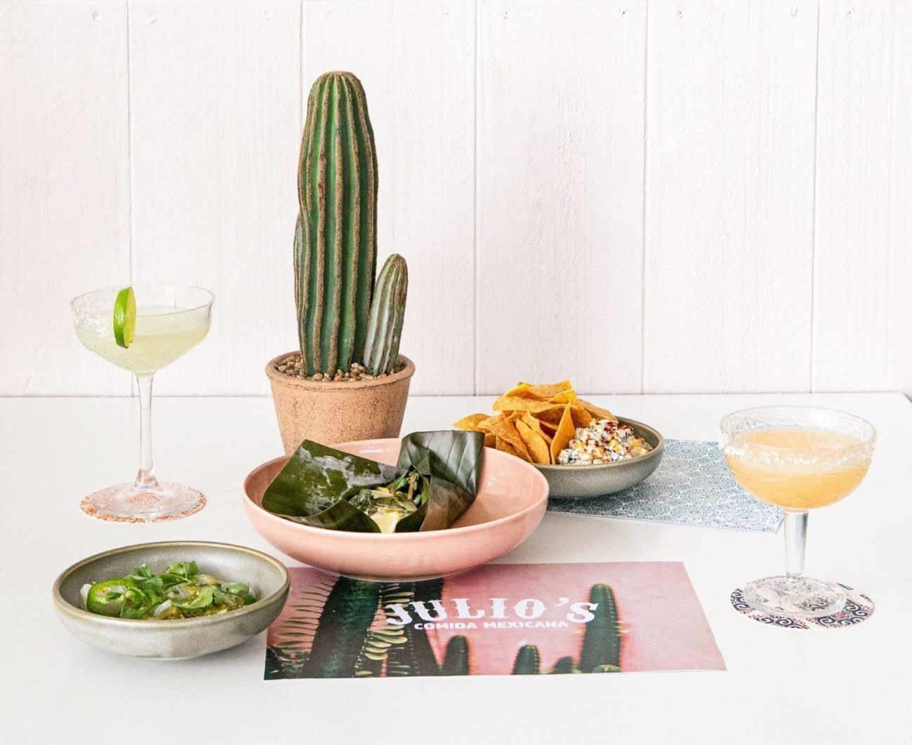 Una mesa con un cactus, un tazón de totopos, una bebida y un plato de comida.