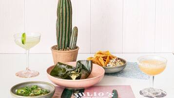 Una mesa con un cactus, un tazón de totopos, una bebida y un plato de comida.