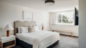 A bedroom with a bed, nightstands, a bench, a TV, and a window with curtains.