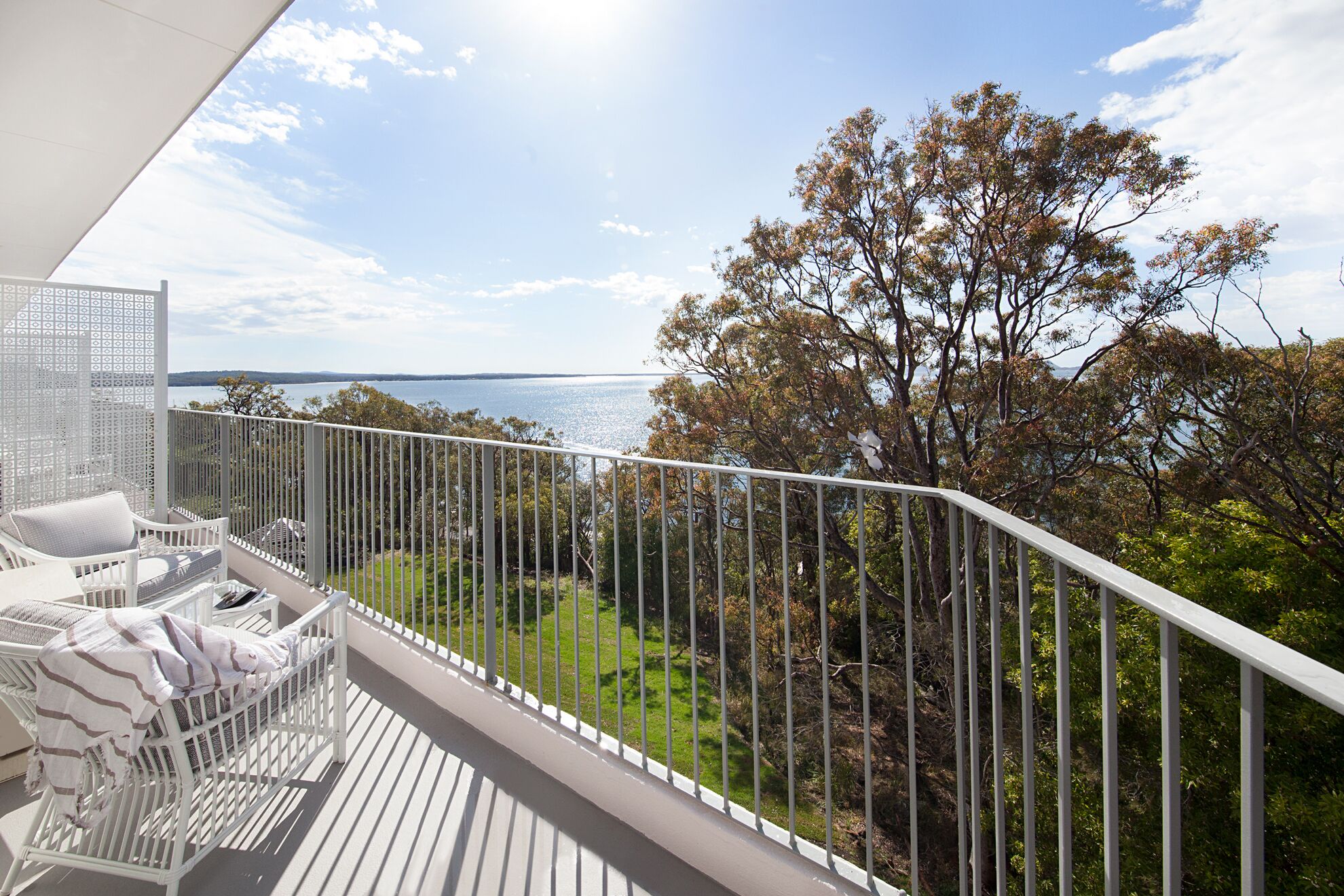Un balcone con mobili bianchi, vista sul mare e un albero sullo sfondo.