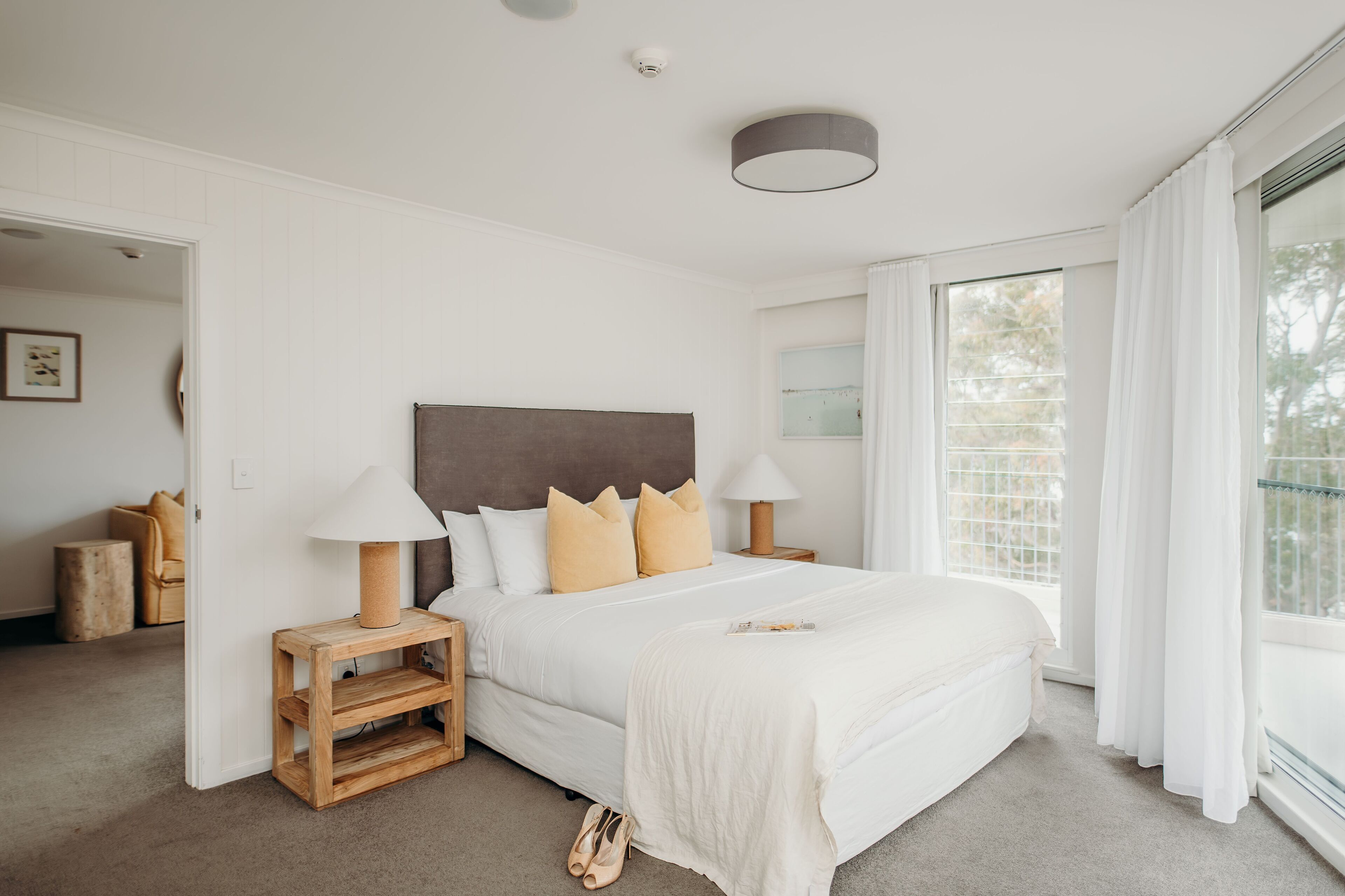 Un dormitorio con una cama grande, mesitas de noche de madera, un cabecero y una ventana con cortinas.
