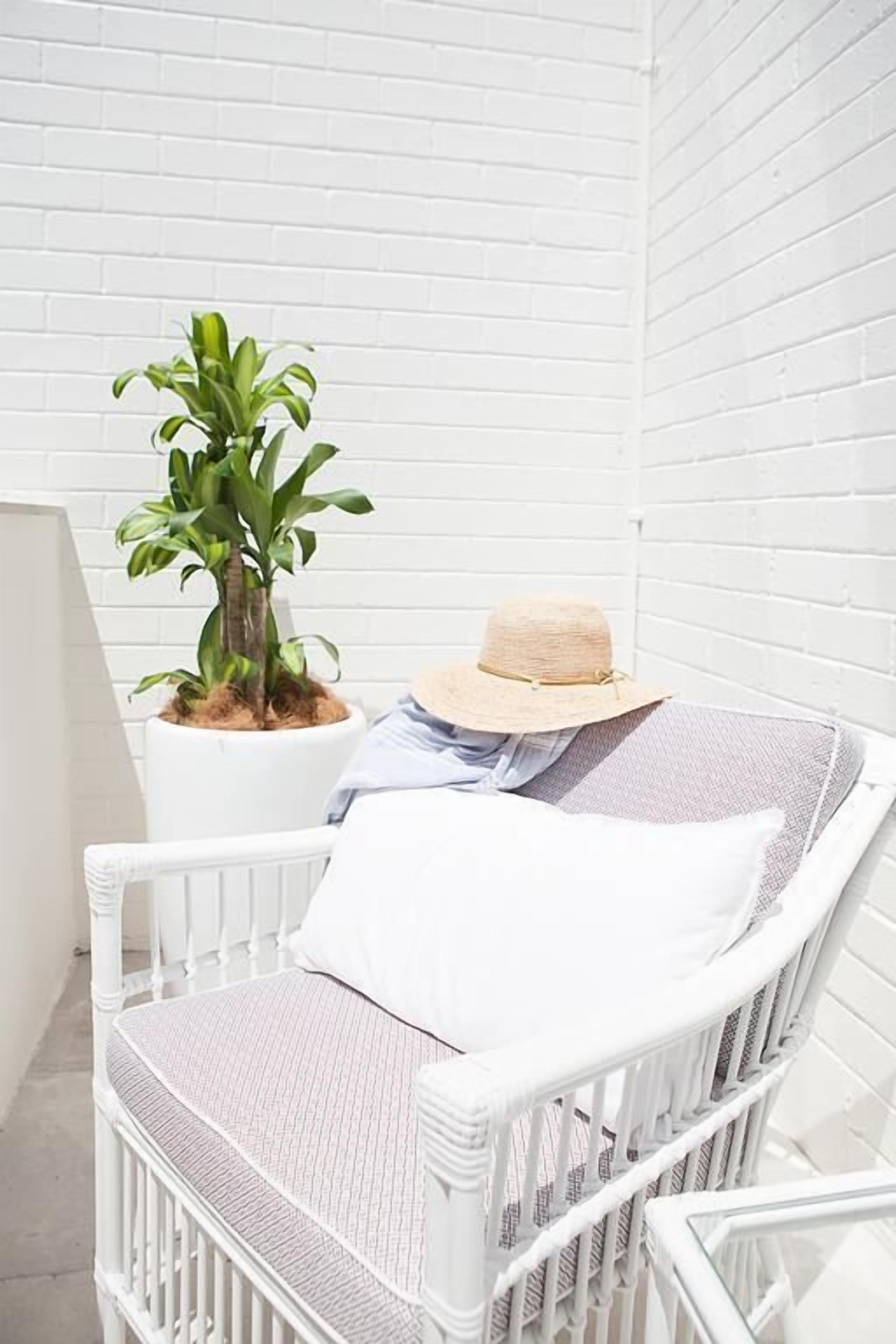 A white wicker chair with a cushion and a straw hat placed on it.