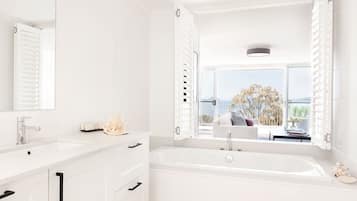 A modern bathroom with a large bathtub, a double sink vanity, and a large window offering a view of the outdoors.