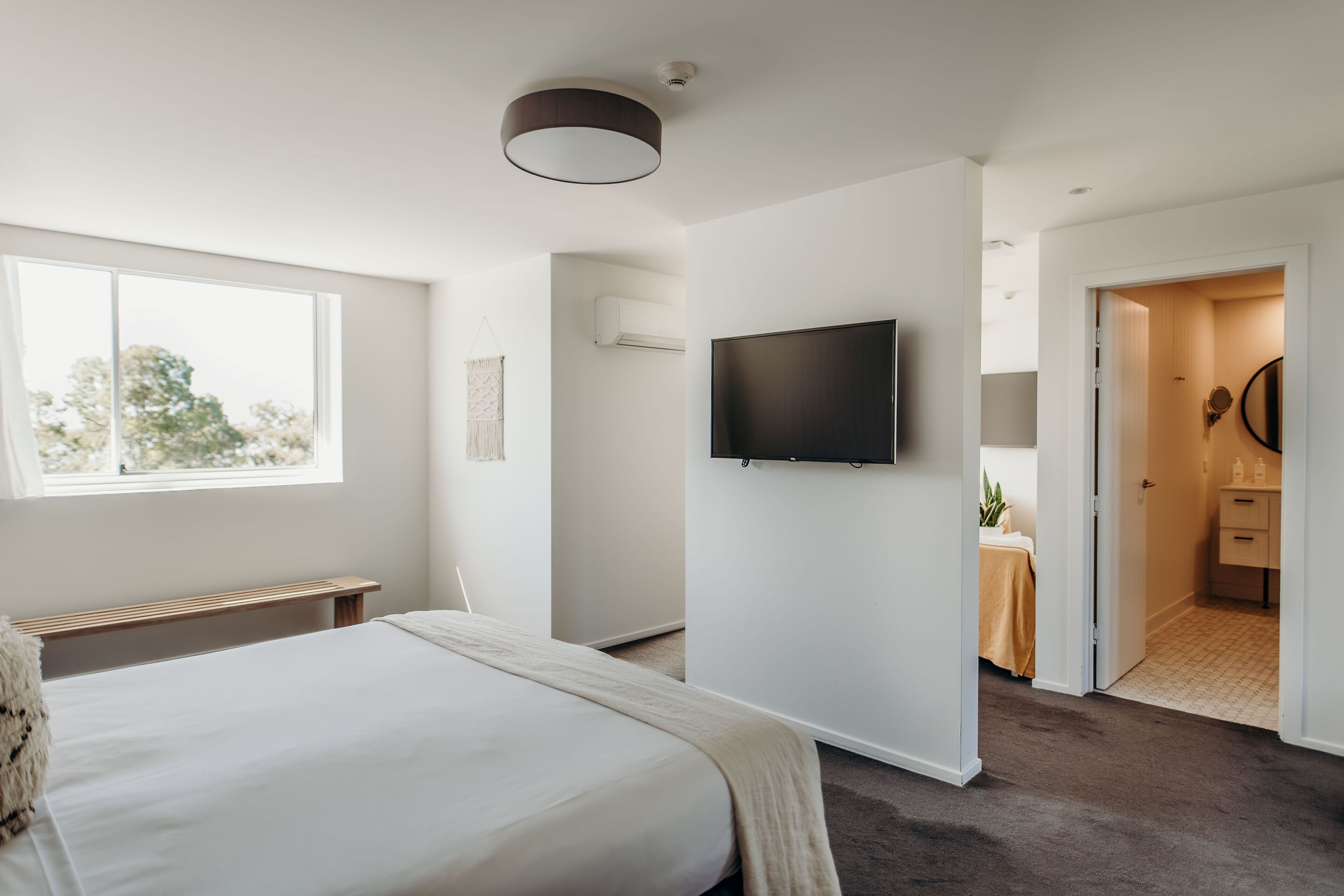 A modern bedroom with a large bed, a mounted TV, and a view of a bathroom through an open door.
