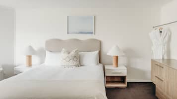 Ein Hotelzimmer mit einem Bett, zwei Nachttischen mit Lampen, einer Holzkommode und einem auf einem Haken aufgehängten Bademantel.