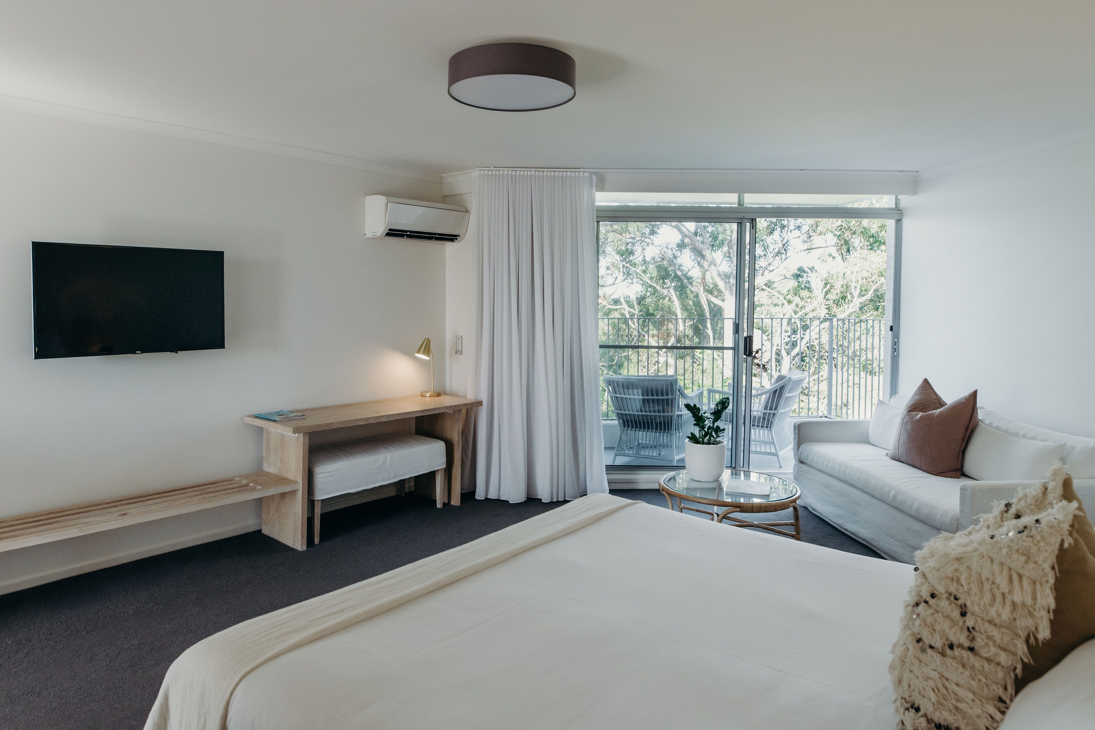 Una habitación de hotel con una cama grande, un escritorio, un televisor, un balcón con vistas a árboles y un sofá.