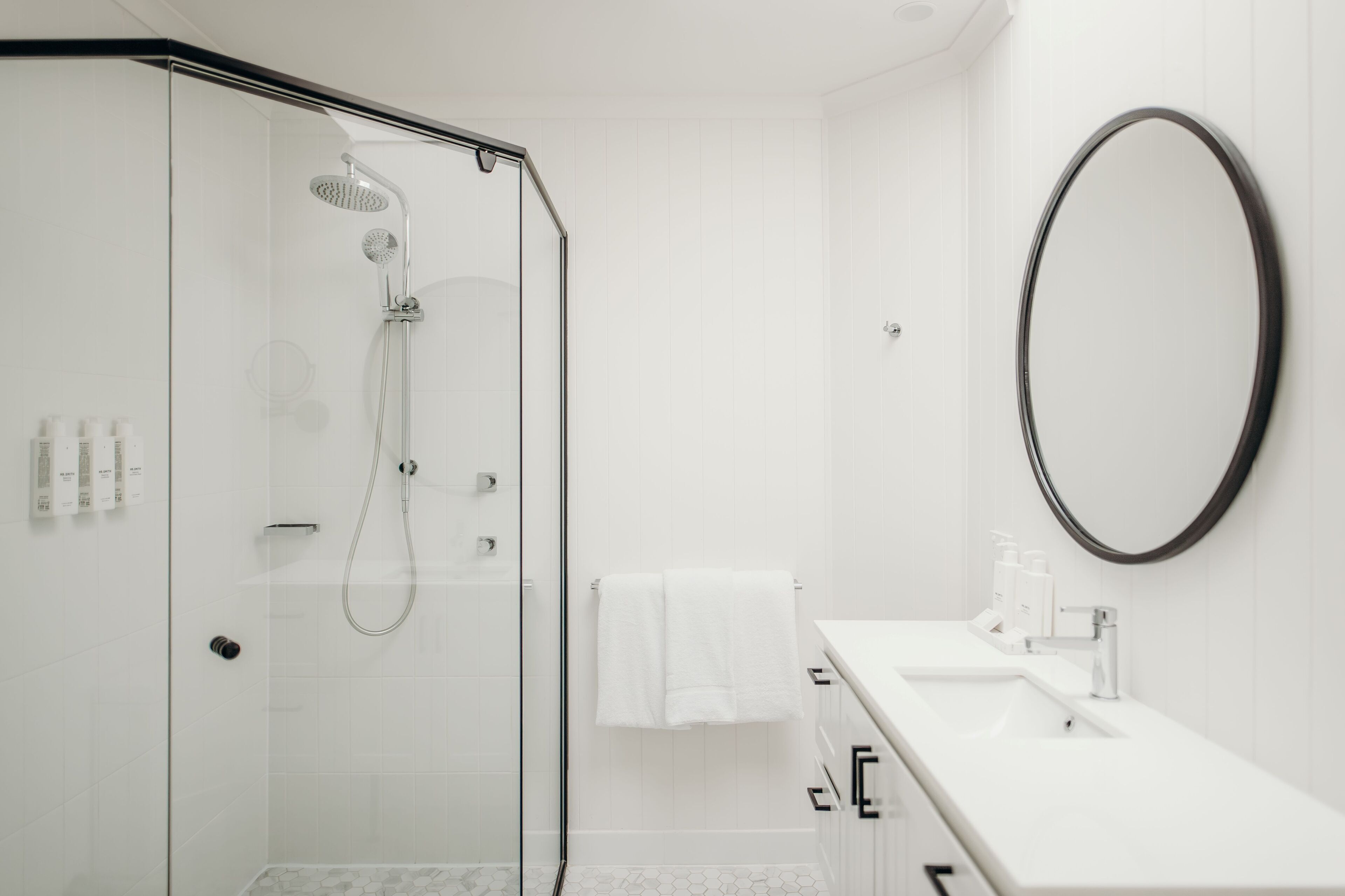 Une salle de bain moderne avec une douche à parois de verre, un lavabo blanc avec un miroir et une serviette blanche accrochée au mur.