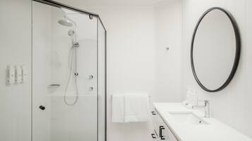 Une salle de bain moderne avec une douche à parois de verre, un lavabo blanc avec un miroir et une serviette blanche accrochée au mur.