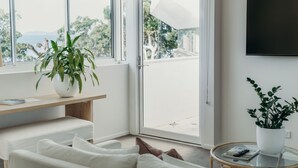 Una sala de estar moderna con un sofá, una mesa redonda de vidrio, una planta en maceta y un televisor en la pared.