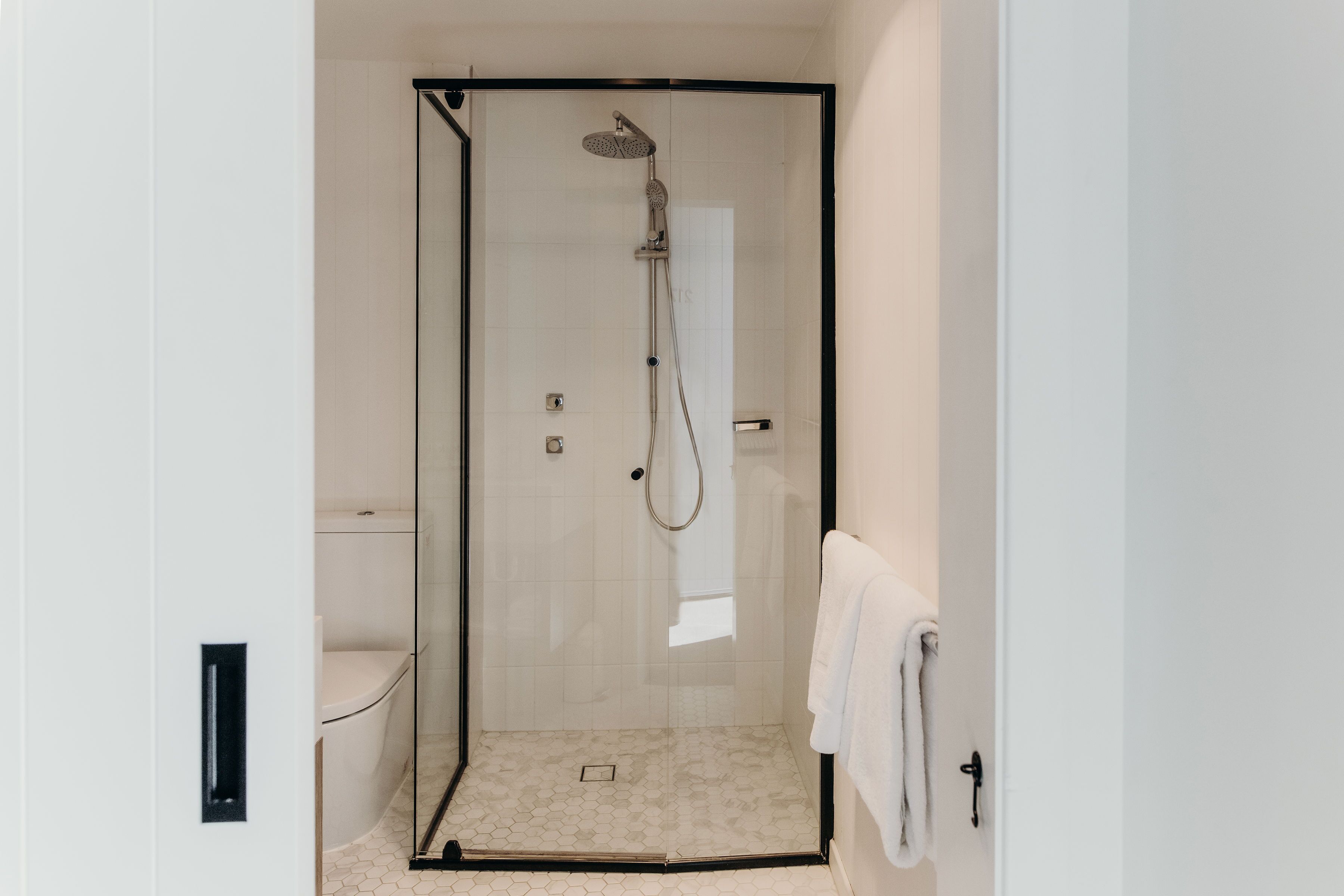 A glass-enclosed shower with a handheld showerhead and a wall-mounted faucet.