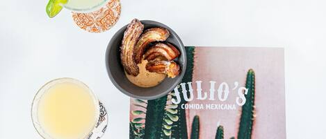 Une table avec des churros, un verre d’une boisson jaune et un livre intitulé « LA CUISINE MEXICAINE DE JULIO ».