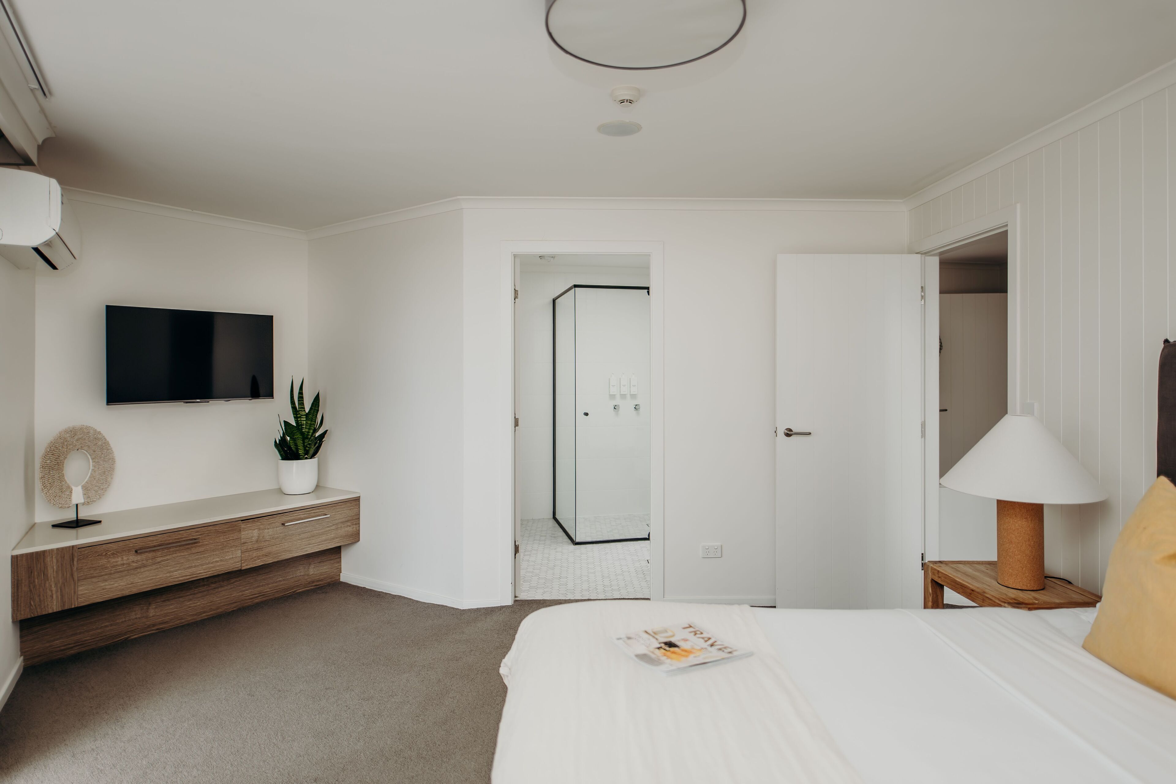 Ein modernes Schlafzimmer mit Bett, Nachttisch, Lampe, Fernseher und begehbarem Kleiderschrank.