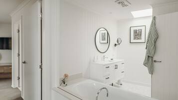 A modern bathroom with a freestanding bathtub, a vanity with a mirror, and a framed picture on the wall.