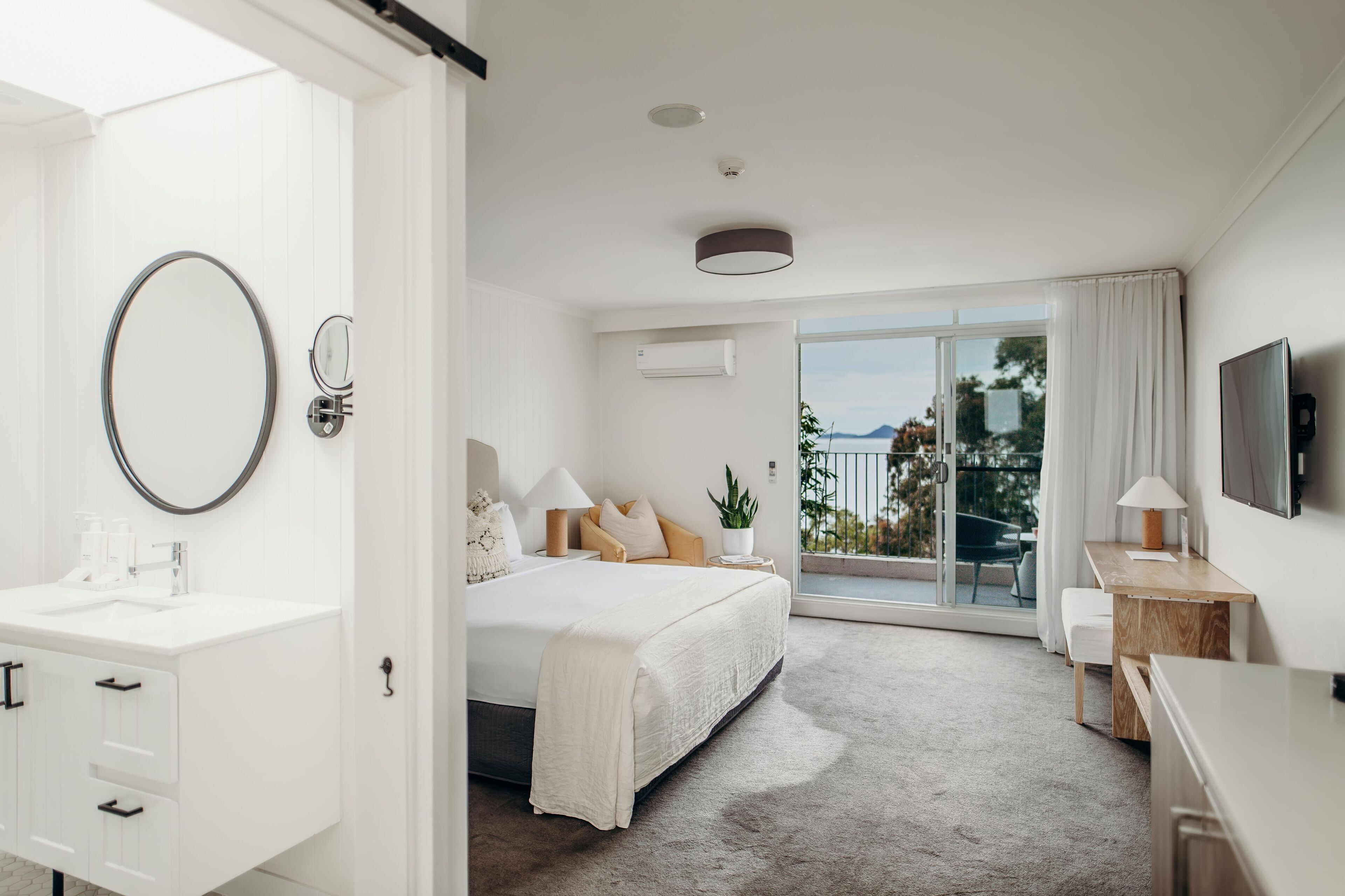 A modern hotel room with a bed, a desk, a TV, and a balcony with a view.