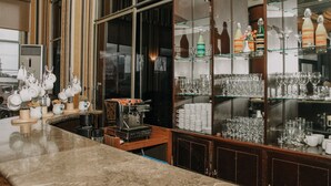 Una zona de bar con una máquina de café, cristalería y una vitrina con botellas y vasos.