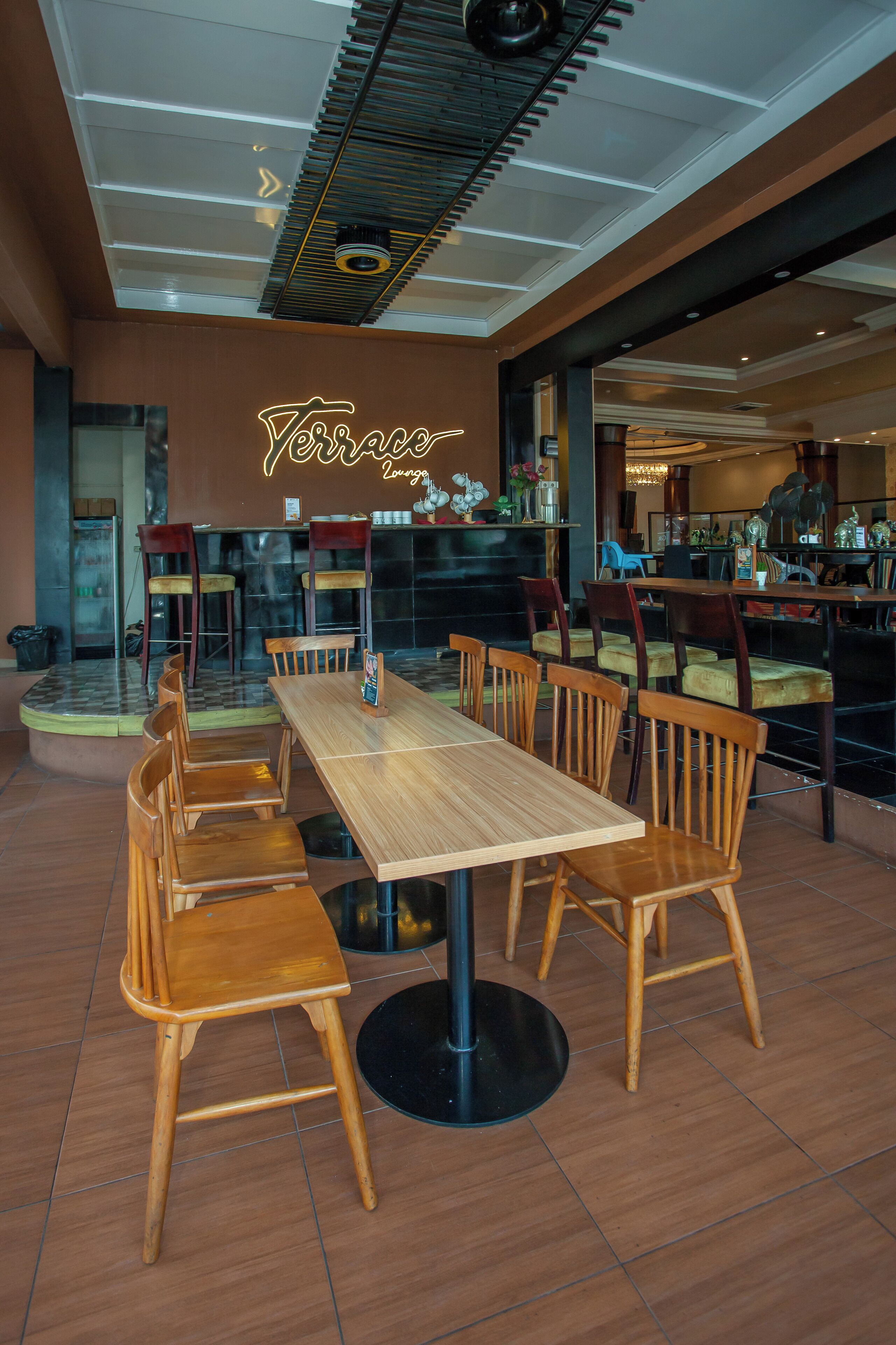 A restaurant with wooden tables and chairs, a neon sign, and a modern ceiling design.