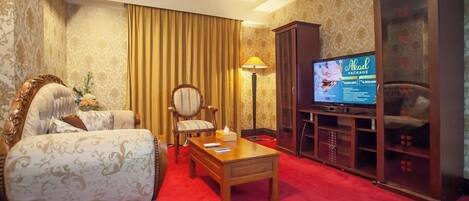 Una habitación de hotel con alfombra roja, una mesa de centro de madera, un sofá, un televisor y un armario.