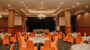 Un salón de banquetes con mesas redondas, sillas anaranjadas y un candelabro.