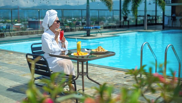 Una persona sentada a una mesa junto a una piscina, con bebidas y comida sobre ella.