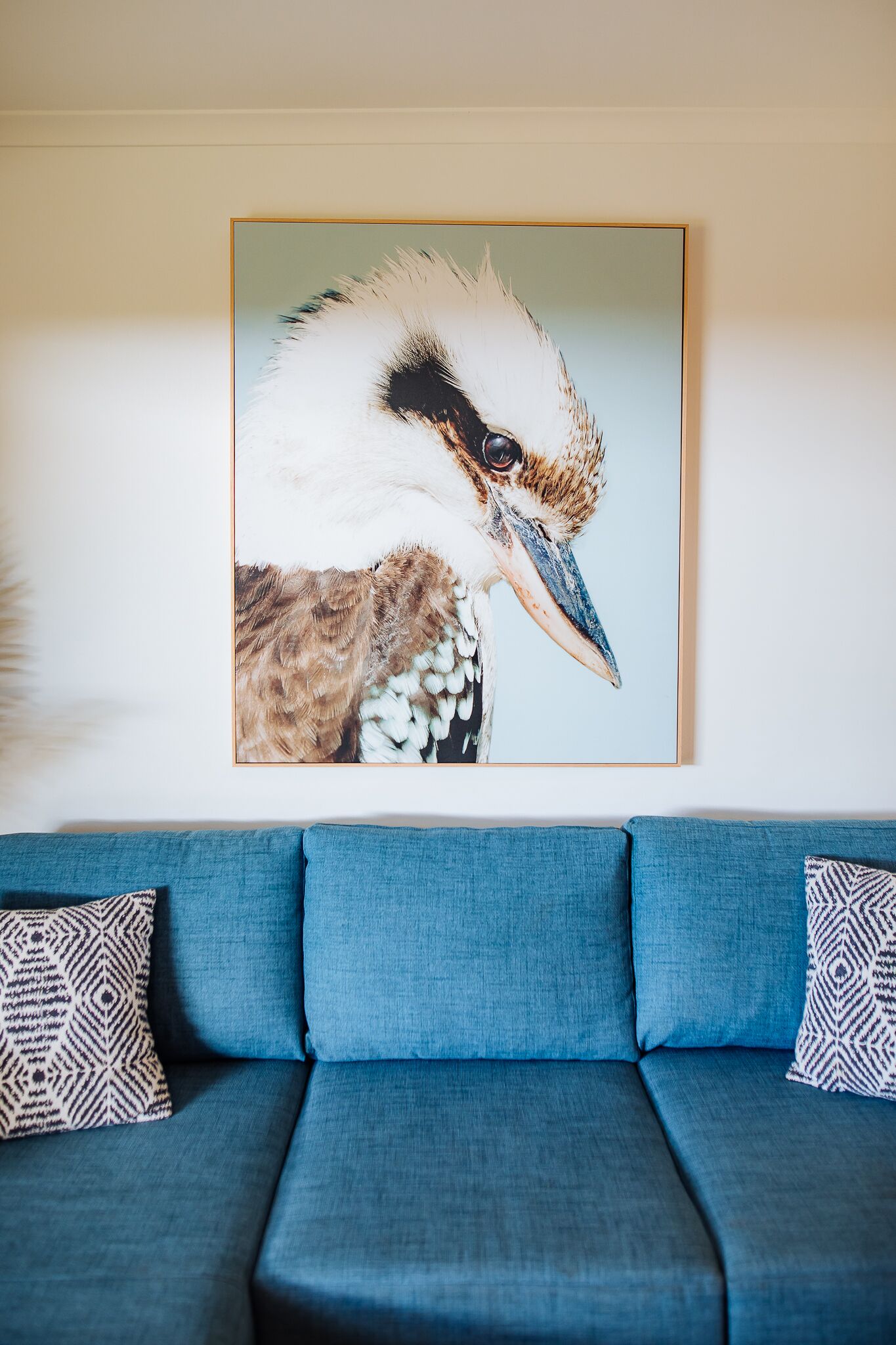 A framed wildlife painting on a wall above a blue sofa with patterned cushions.