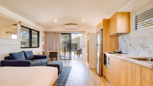 Ein modernes Hotelzimmer mit Bett, einer Sitzecke, einer Küchenzeile inklusive Kühlschrank und einer Schiebetür zu einem Sitzbereich im Freien.