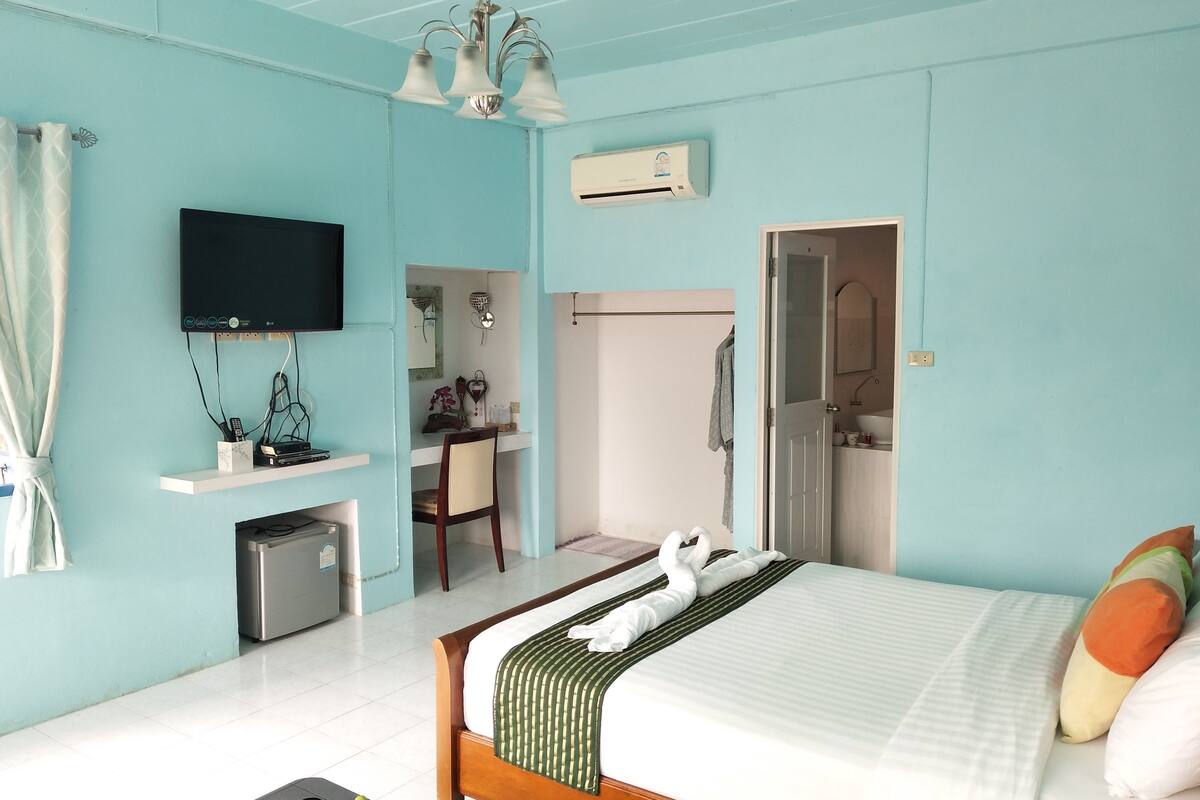 A hotel room with a bed, a desk, a TV, an air conditioner, and a bathroom.