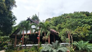Edifici de fusta tradicional amb teulada d'àmples rajoles, envoltat de vegetació abundant i plantes en test.