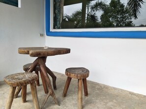 A rustic wooden table with a stool and a smaller stool beside it, set against a white wall with a blue trim and a window overlooking palm trees. - Mountain Beach  Resort (Rayong)