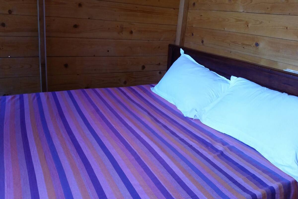 Un lit recouvert d’une couvre-lit à rayures et orné d’oreillers blancs, dans une pièce aux murs en bois.