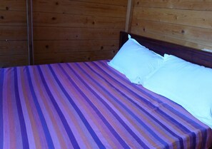 Un lit recouvert d’une couvre-lit à rayures et orné d’oreillers blancs, dans une pièce aux murs en bois.