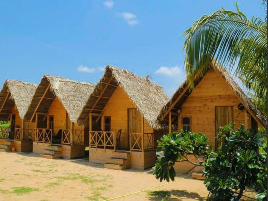 Fileira de casas de campo com telhados de palha, paredes de madeira e chão de areia.