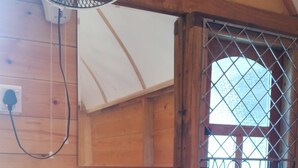 L’intérieur d’une cabane en bois, avec une seule fenêtre, une petite boîte en bois et un ventilateur fixé au mur.