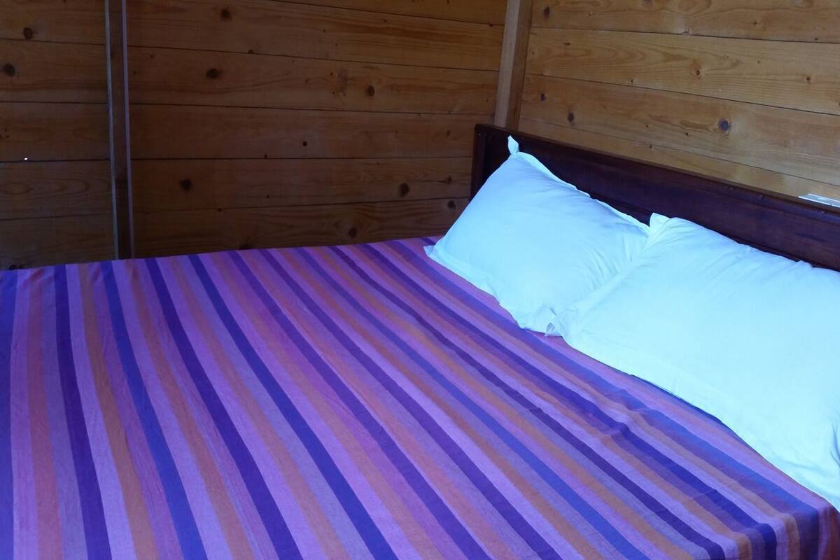 Un lit avec une couvre-lit à rayures et des oreillers blancs, dans une pièce aux murs en bois.
