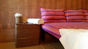 Un lit bien fait, avec une literie à rayures, une petite table de chevet sur laquelle se trouve une boîte de mouchoirs et une serviette enroulée.