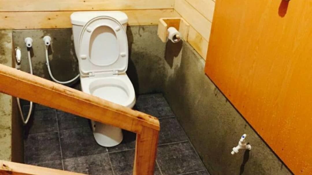 Ein kleines, kompaktes Badezimmer mit Toilette, einer Holzbank und einem fest montierten Toilettenpapierhalter.