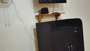 Une pièce avec un téléviseur fixé au mur, une petite étagère sur laquelle se trouve un appareil, et un meuble.