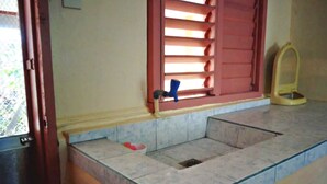 Une salle de bain avec un sol carrelé, une fenêtre avec des stores rouges et des toilettes.