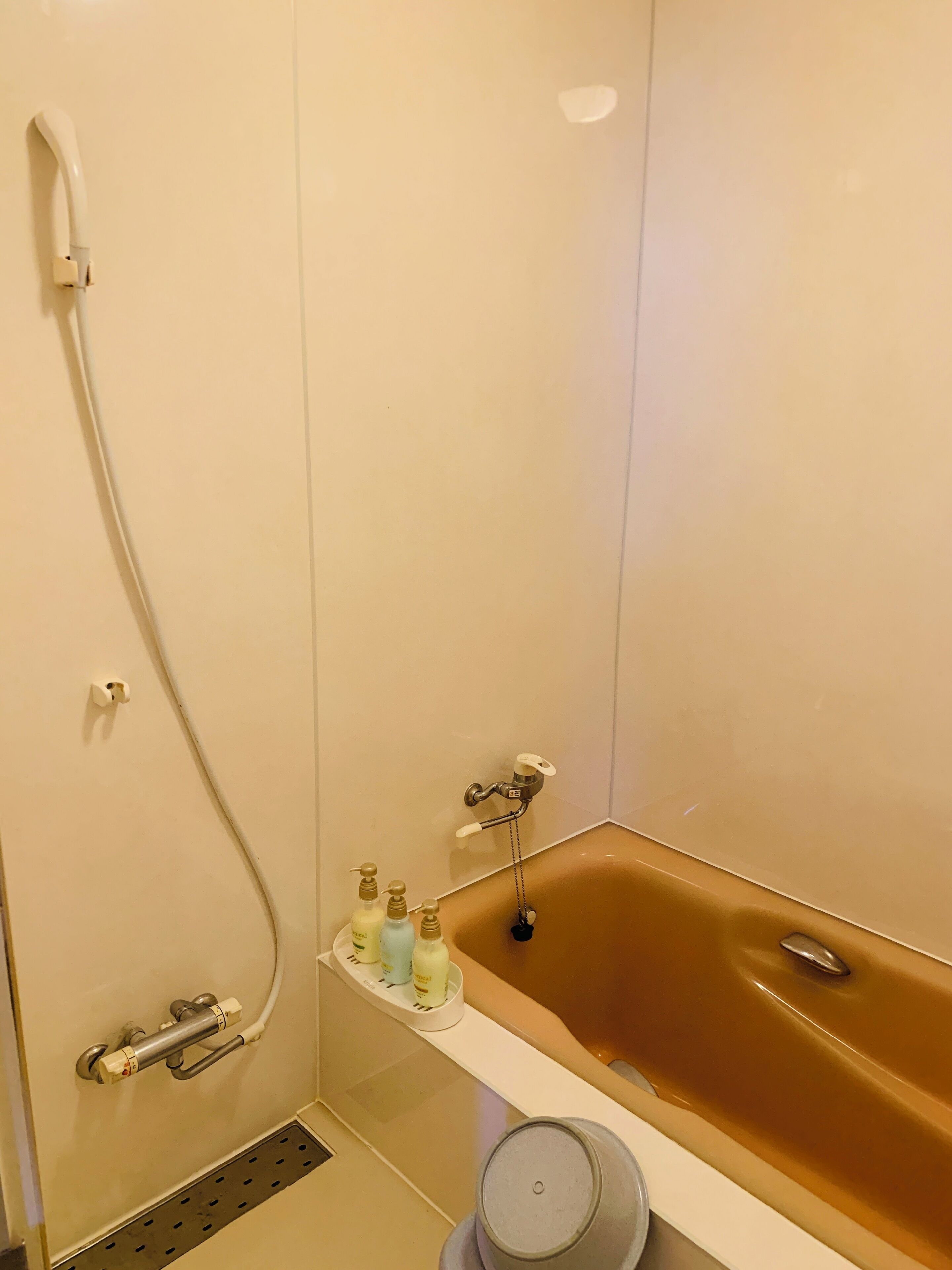 A bathroom with a bathtub, a showerhead, and a shelf with toiletries.