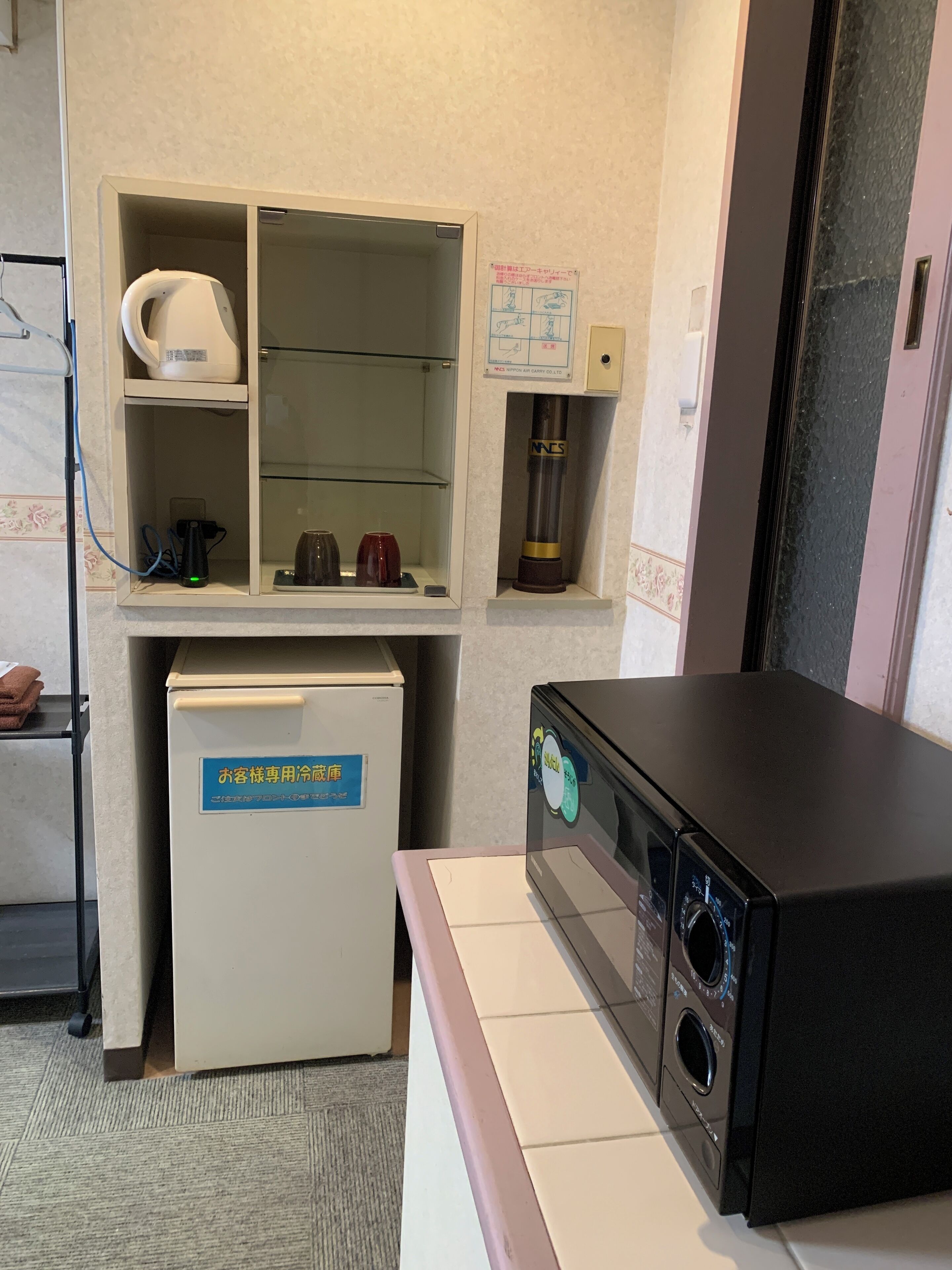 Une chambre d’hôtel équipée d’un mini-bar, d’un réfrigérateur, d’un four à micro-ondes et d’un petit meuble contenant une bouilloire et des tasses.