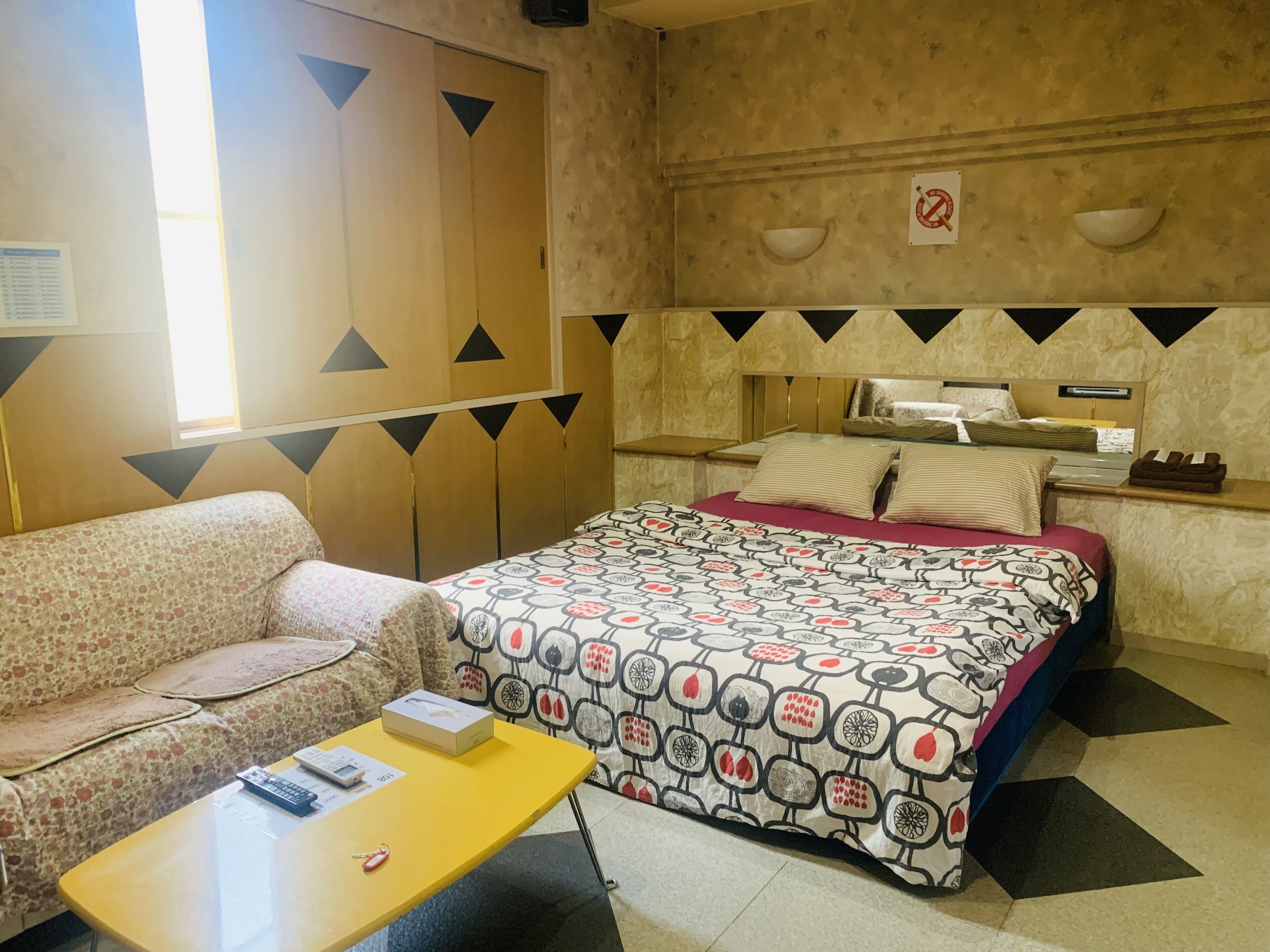 Una camera d'albergo con un letto, un divano, un tavolino e una parete con motivo geometrico.
