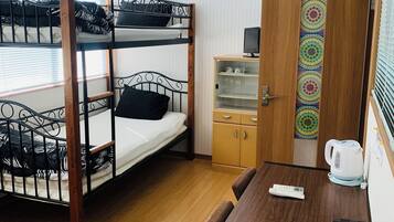 A bunk bed room with a wooden table, a small cabinet, and a door with a number sign.