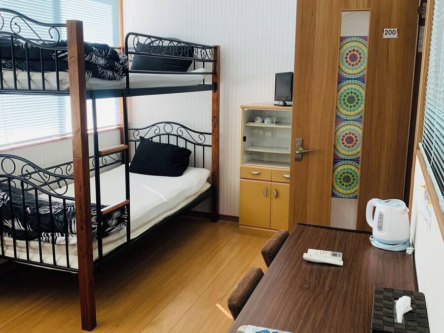 A bunk bed room with a wooden table, a small cabinet, and a door with a number sign.