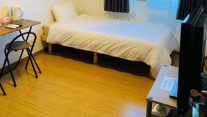 A hotel room with a bed, a desk with a chair, a television, and an air conditioning unit. - villageBFH - Hostel (Omura)