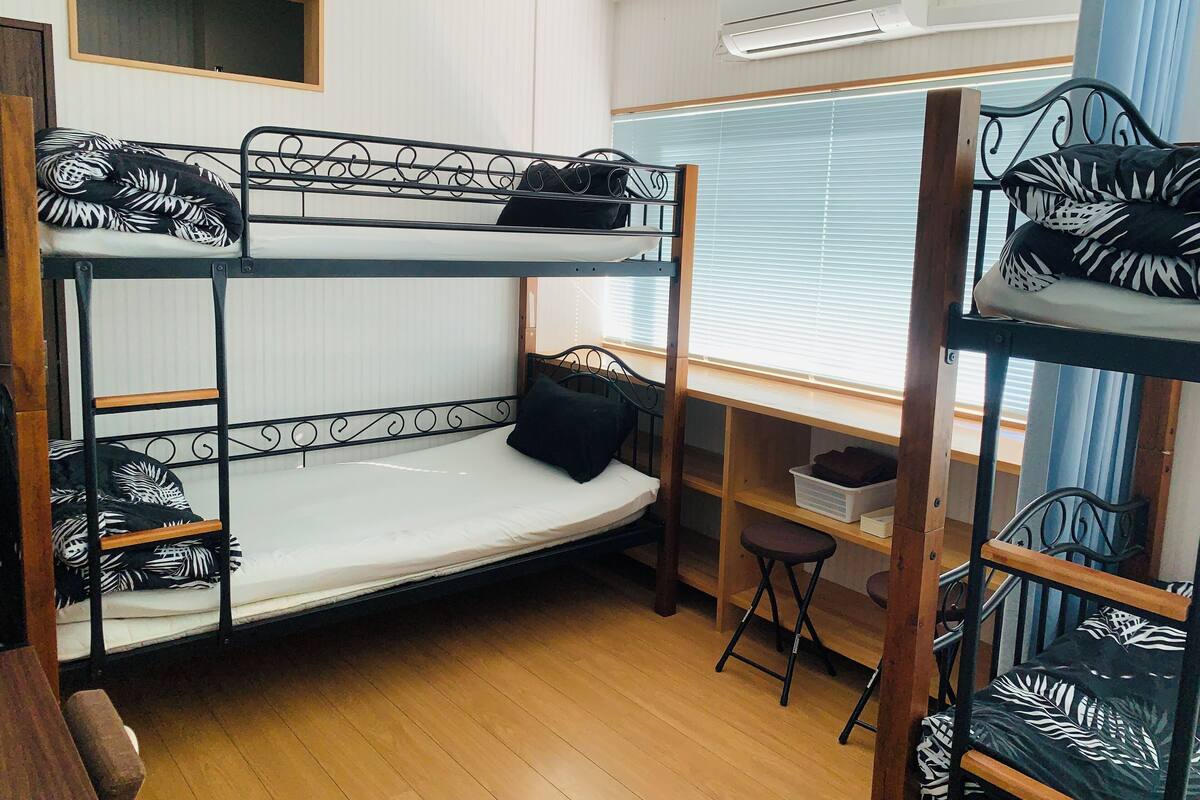 A bunk bed room with a desk and chair, a window with blinds, and an air conditioning unit.